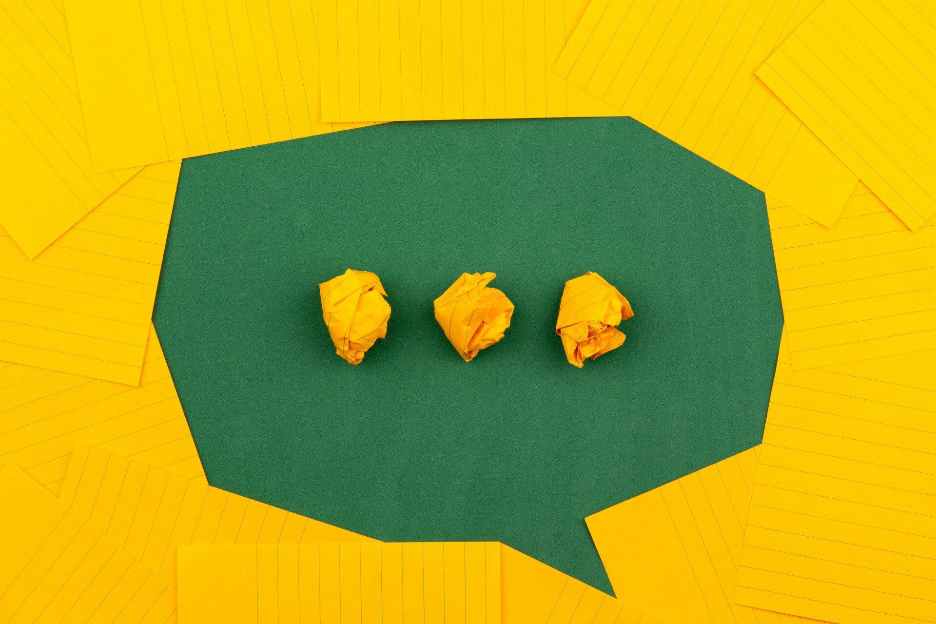A green paper speech bubble on a yellow paper background.